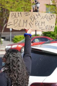 A protestor holds up a sign that says "BLM," "I can't breathe," and "Don't shoot."