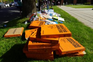 A pile of pizza boxes, water bottles, and food sits behind the protestors.