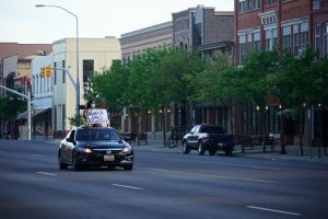 A protestor holding a "Black Lives Matter" poster sits on top of a car as it drives down Main Street in Logan, UT.