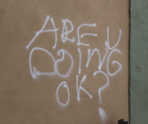 A photograph of grafiti on a wall outside that says "Are u doing ok?"