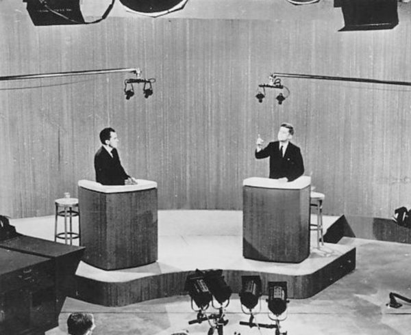Democratic nominee John F. Kennedy gestures as Republican nominee Richard Nixon watches him from the other podium on the debate stage. The two are standing at reciprocal podiums on a stage in an ABC studio in 1960.